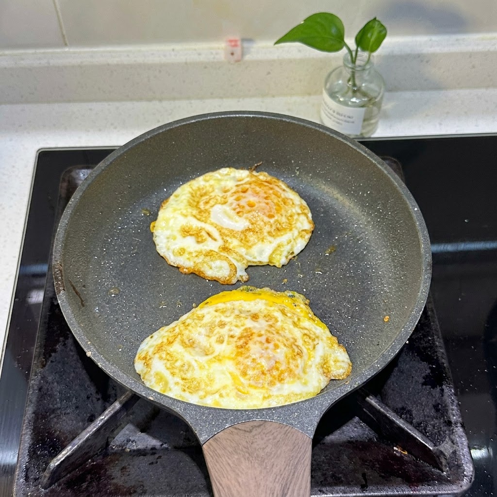 Two fried eggs cooking in a pan with golden-brown edges.