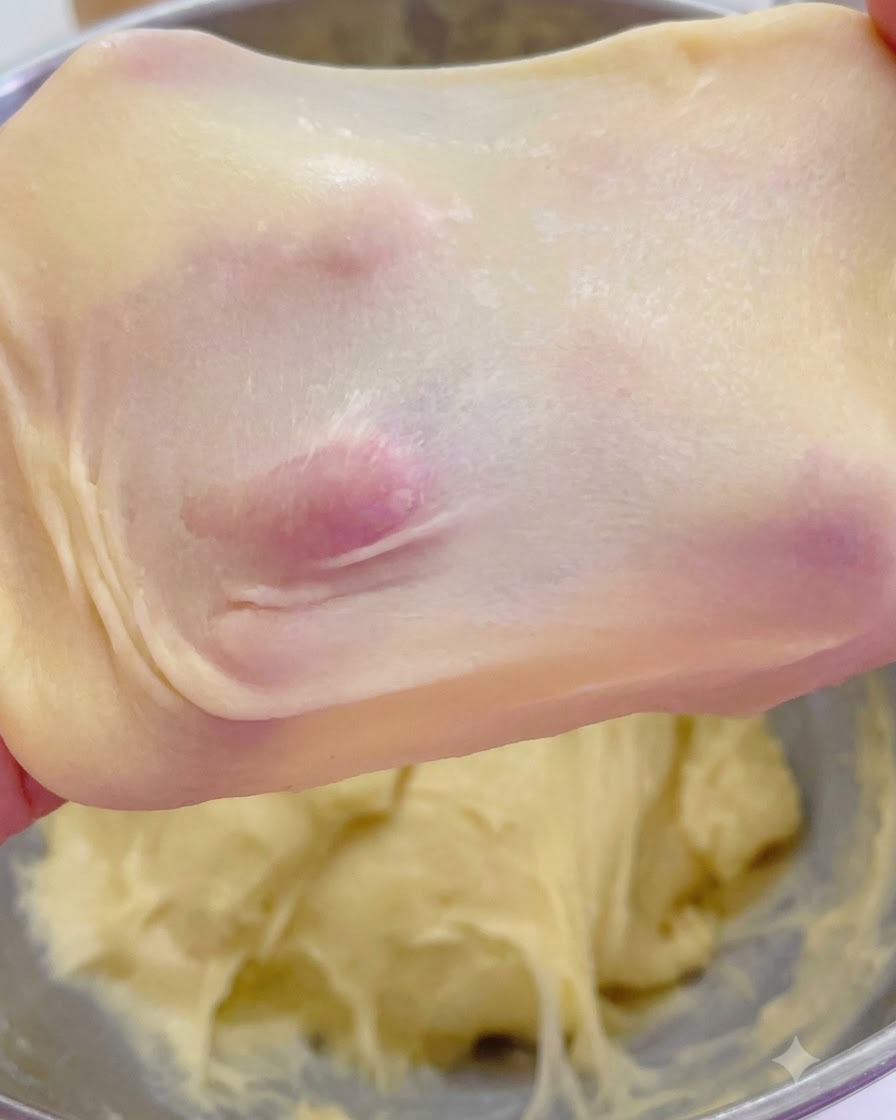 Stretched brioche dough showing a thin, translucent windowpane membrane held up by fingers.