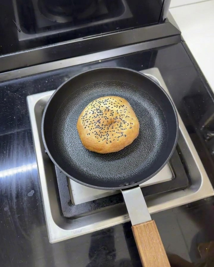A butter burger bun sitting in a frying pan with water around it, ready to be steamed with a lid.
