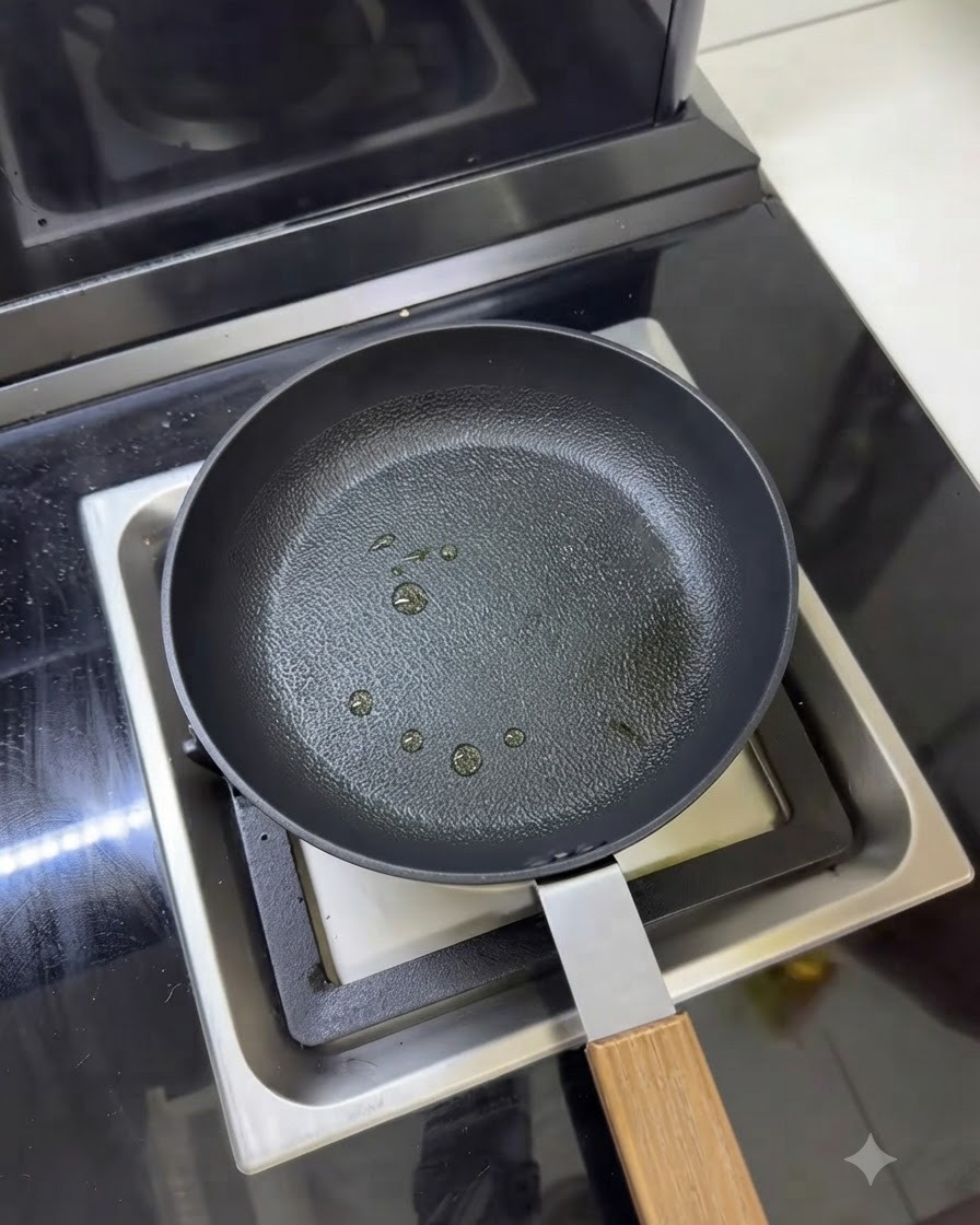 A frying pan with several small droplets of cooking oil sprayed on the surface.