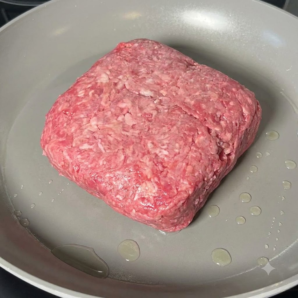 Ground beef being cooked and broken down with a wooden spatula in a wide frying pan.