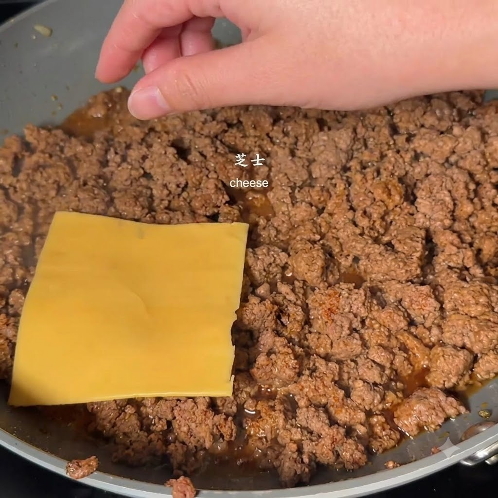 A yellow square cheese slice being placed on top of cooked minced beef in a pan by a hand.