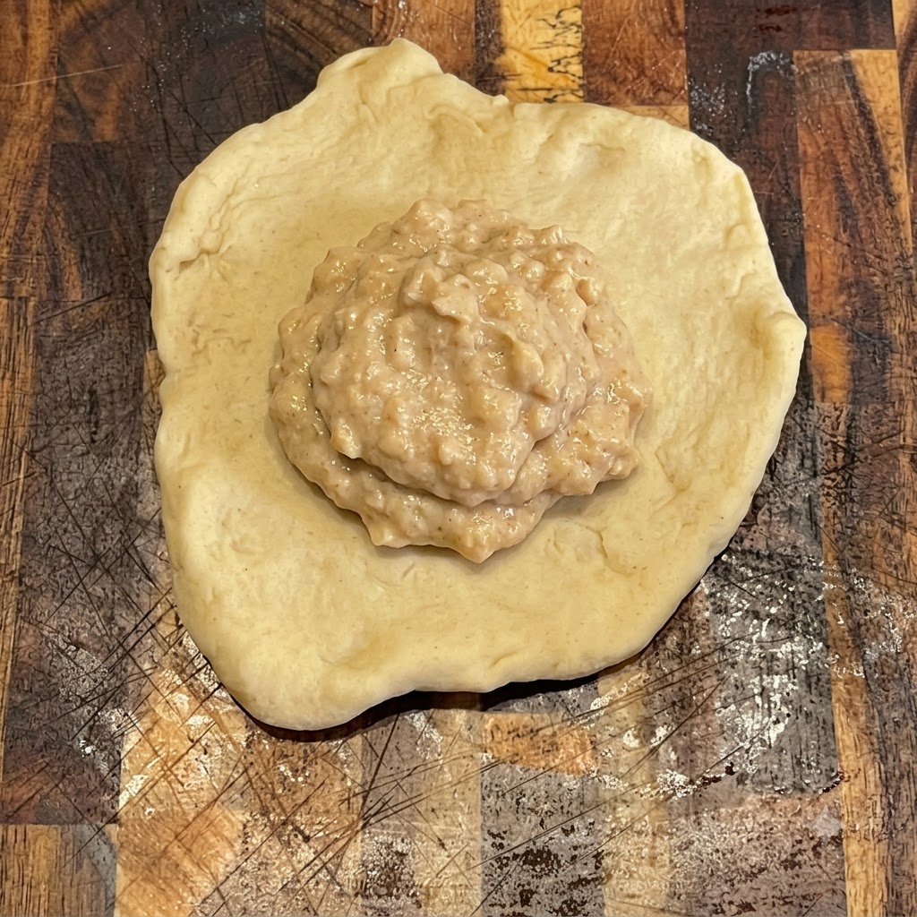 Burger sauce spread neatly on top of a flat round piece of dough on a wooden board.