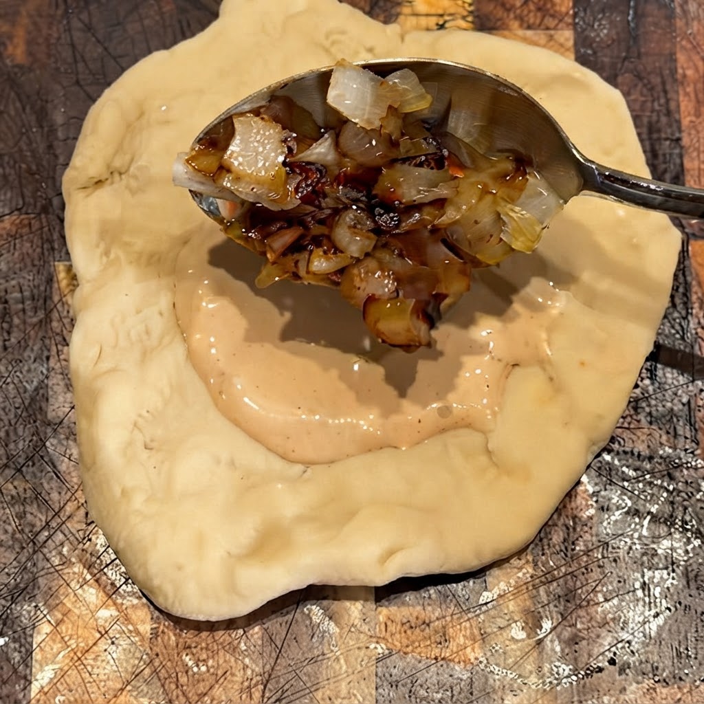 Grilled onions being spooned on top of the sauce layer on the dough.
