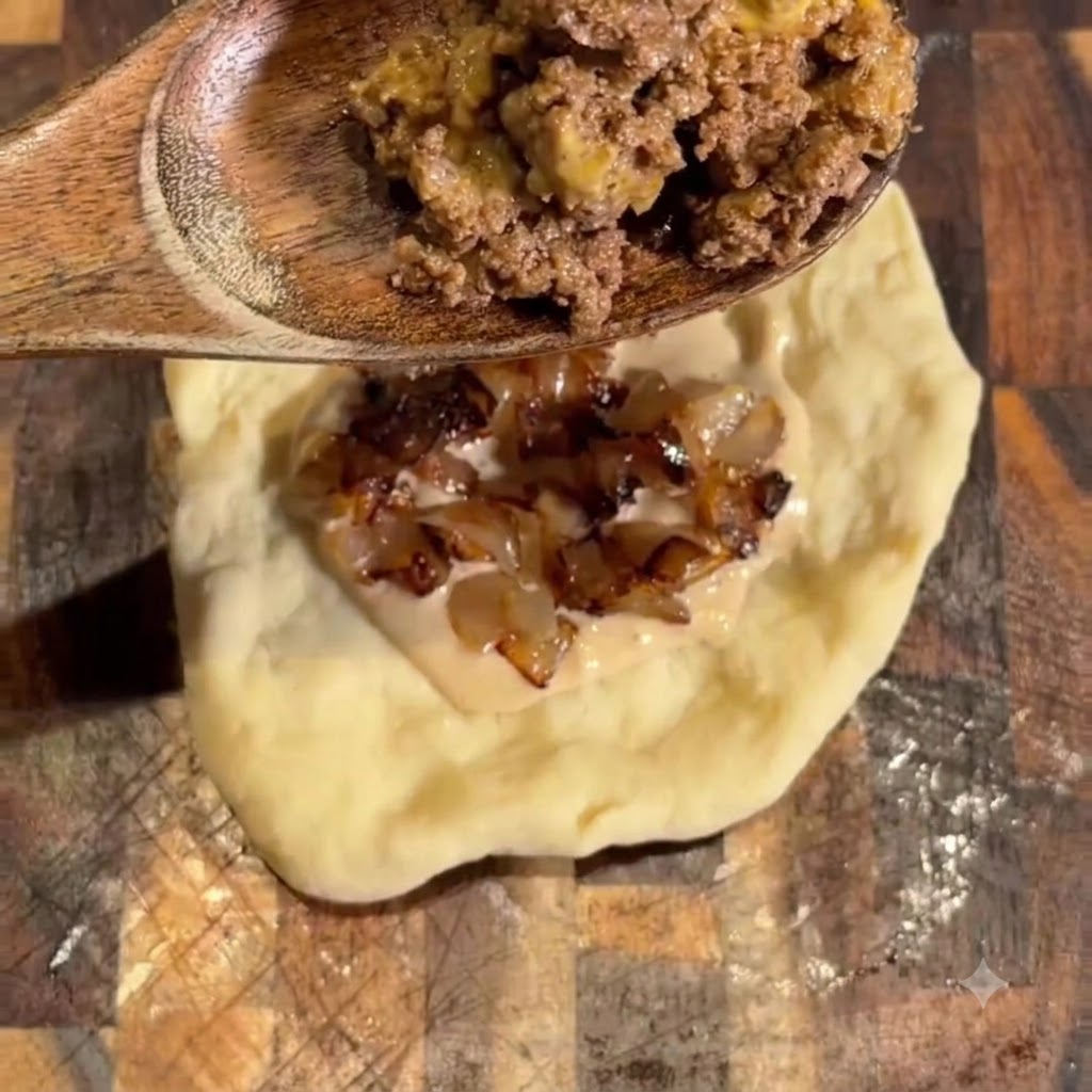 Cooked ground beef being added with a wooden spoon over the onions and sauce.