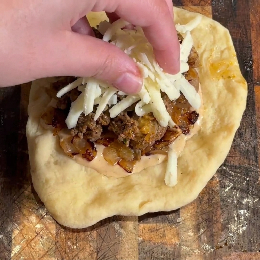 Shredded mozzarella cheese being sprinkled on top of the burger filling.