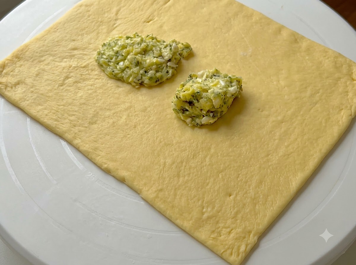 Dollops of green garlic butter spread sitting on top of a flattened rectangular sheet of dough.