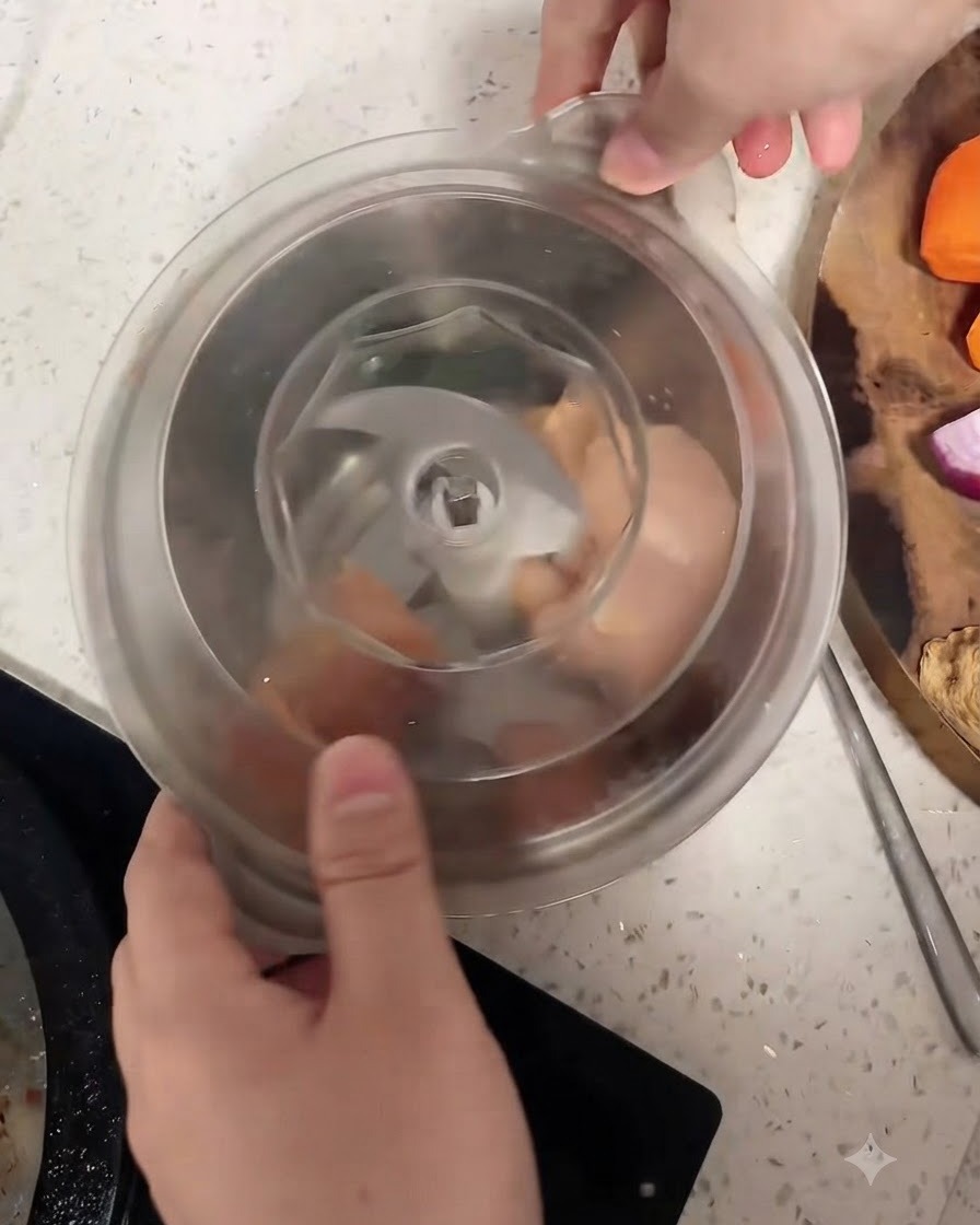 Raw chicken breast pieces inside a food processor bowl surrounding the central blade.