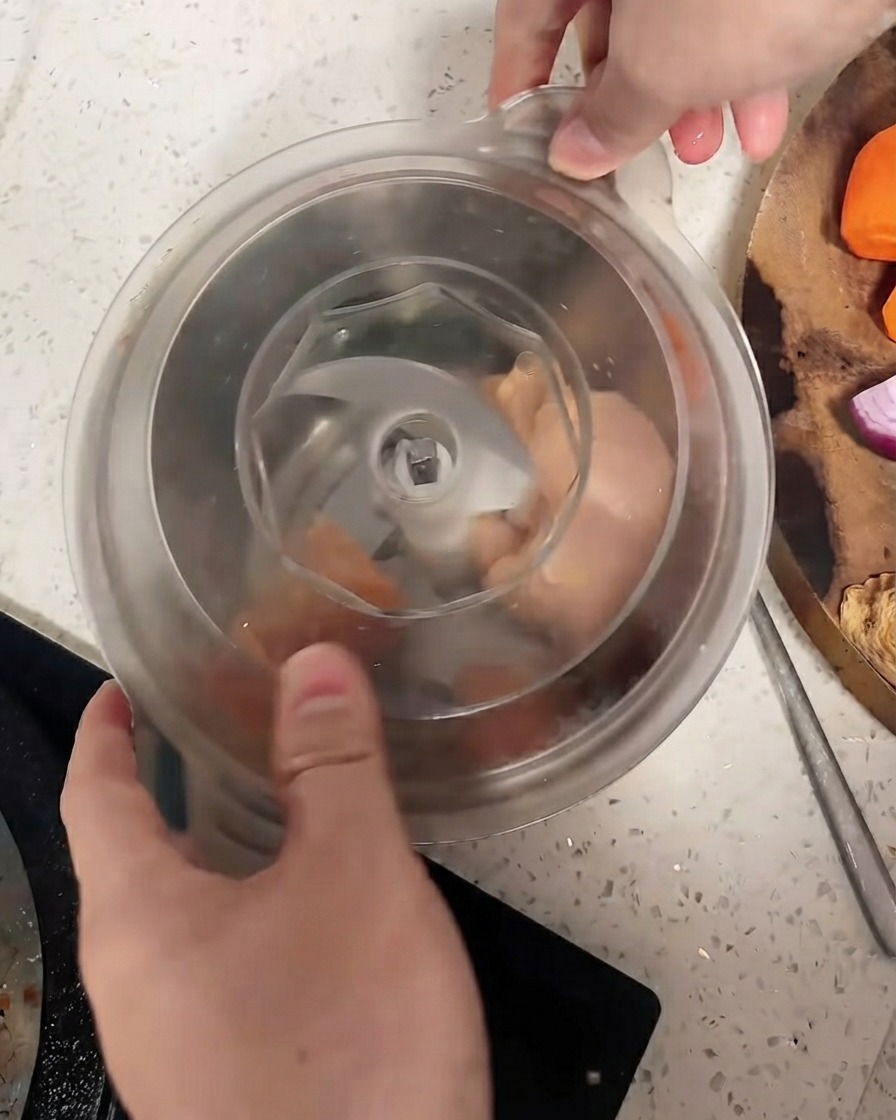 A food processor with its lid secured over chicken pieces.