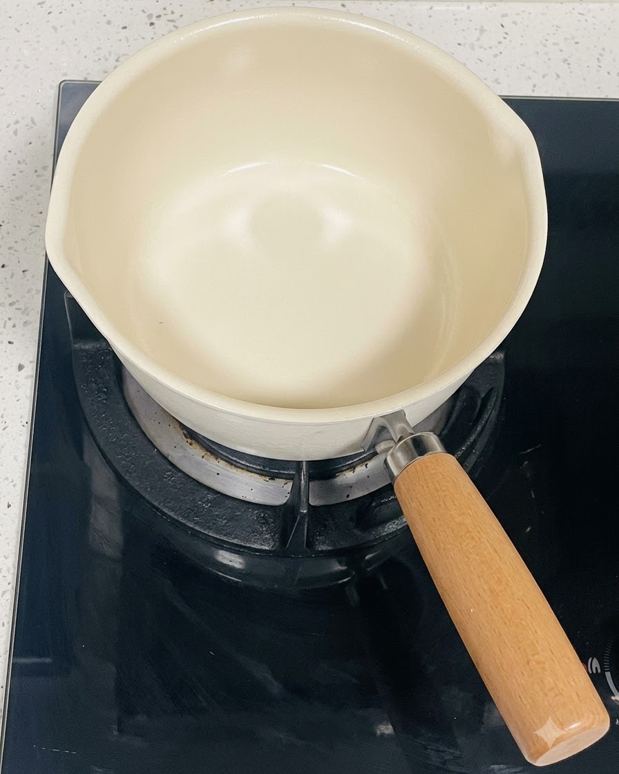An empty cream-colored cooking pot sitting on a black induction stovetop burner.