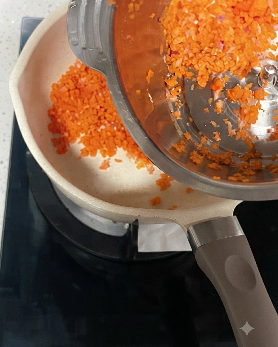 Minced carrots and onions being poured from a steel container into a heated pot.