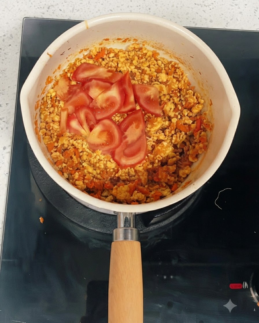 Fresh tomato slices resting on top of the cooked chicken and vegetable mixture in a pan.