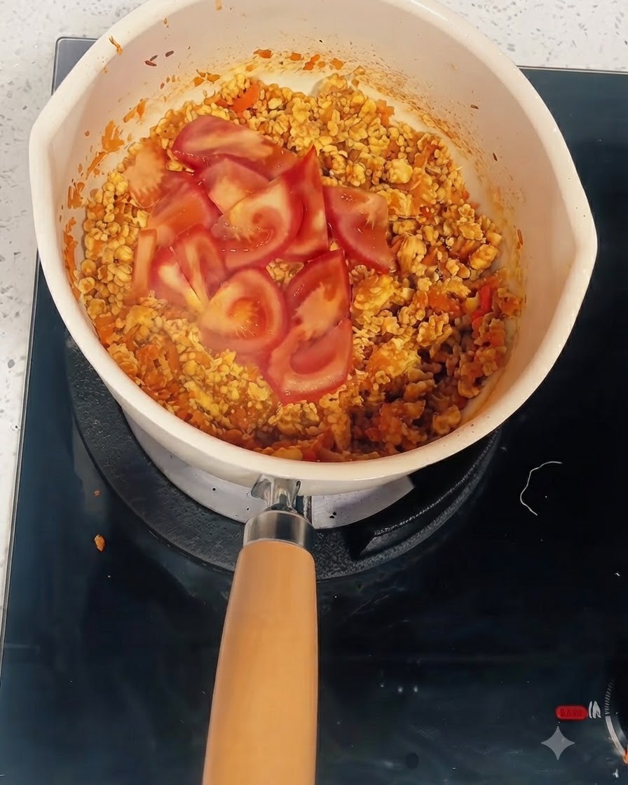 Tomato slices over the cooked mixture in a pot where water and tomato paste are added.