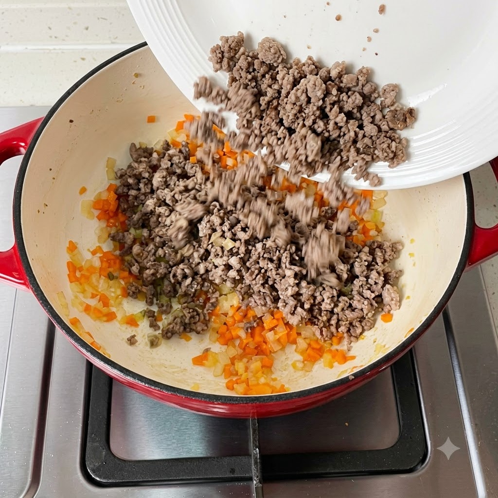 Cooked minced meat being added back into the pan containing vegetables.