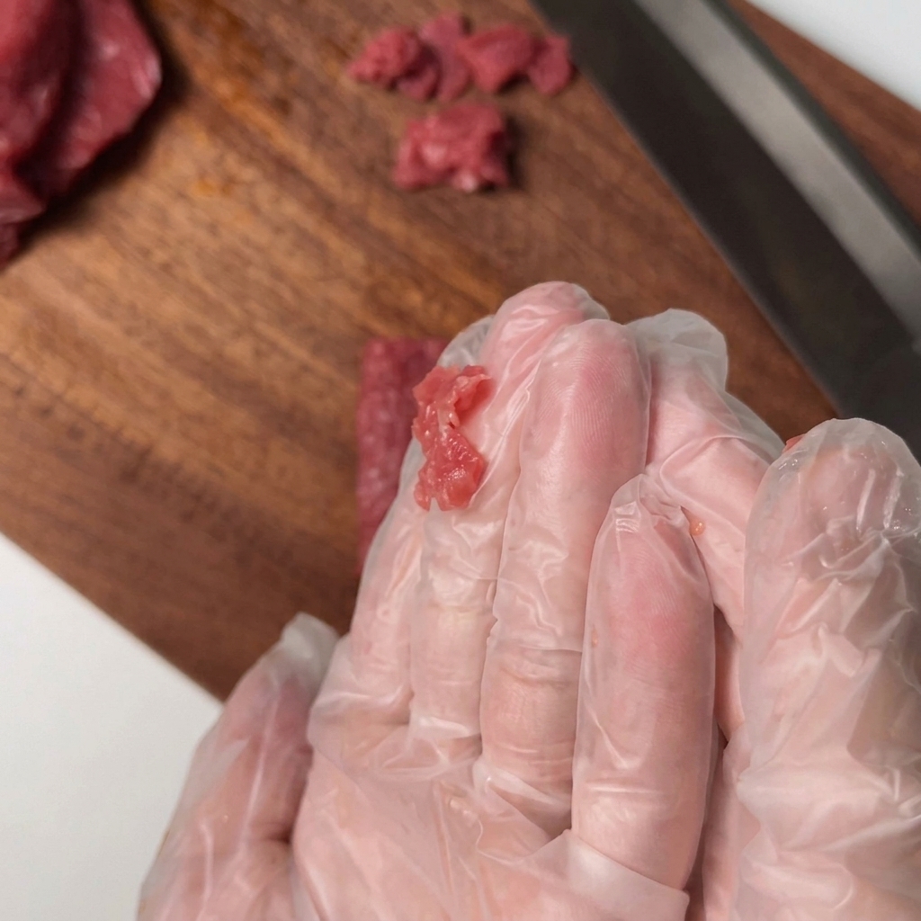Sliced beef tenderloin being hand-mixed with seasonings in a bowl.