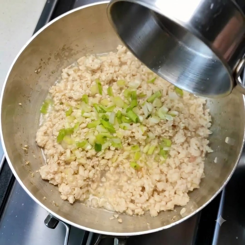 Chopped green onions and garlic scattered over cooked minced chicken inside a pan.
