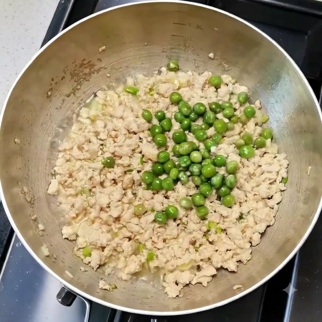 Green peas mixed evenly with chicken and aromatics in a cooking pan.