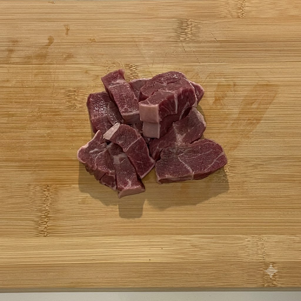 Chunks of raw beef loaded into a steel food processor bowl.