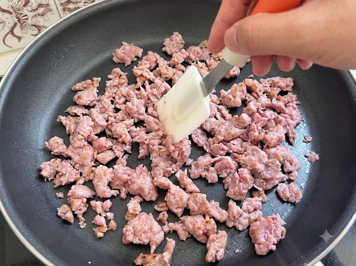Italian sausage meat being actively stirred and fried with a spatula in a pan.