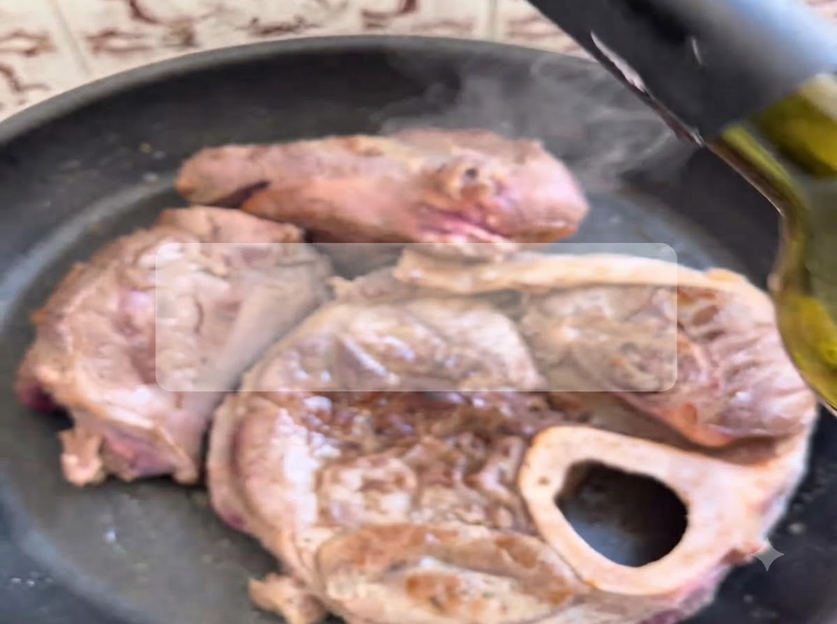 Red wine being poured from a bottle onto seared beef cuts sizzling in a hot pan.