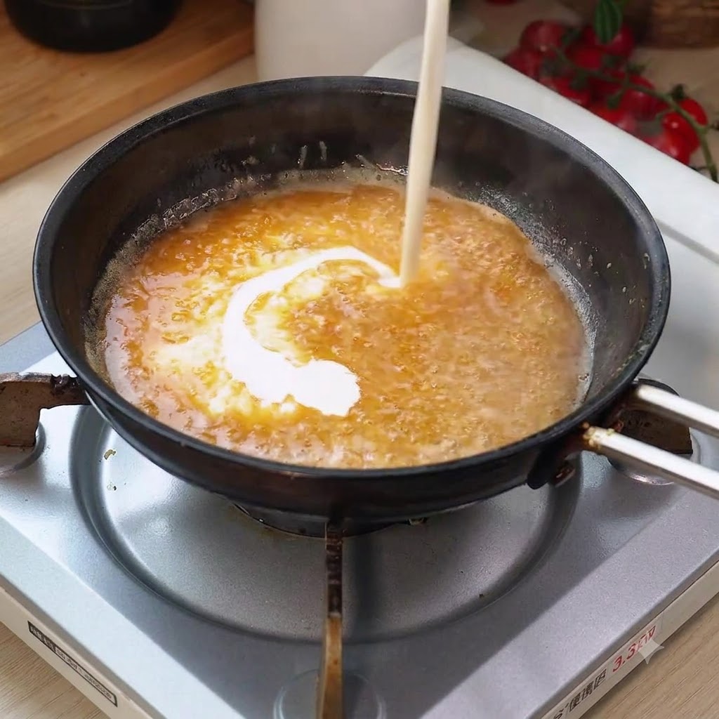 Heavy cream being poured into the bubbling pan sauce, creating a swirling blend.