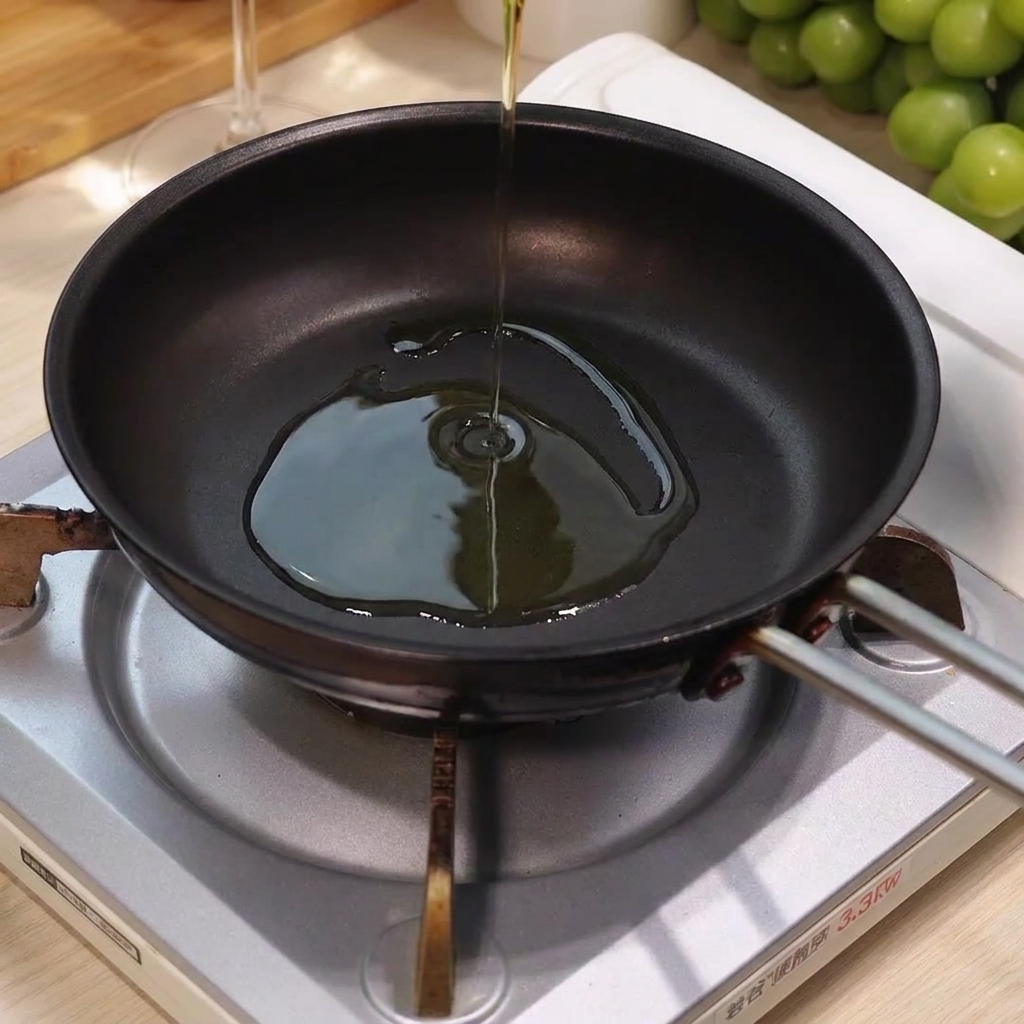 Olive oil being poured into the center of a hot, empty frying pan on a burner.