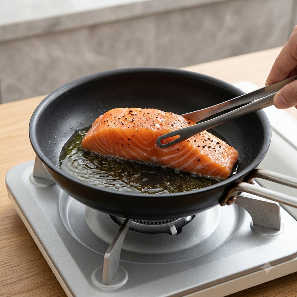 A fresh salmon fillet being placed skin-side down into a hot frying pan using kitchen tongs.