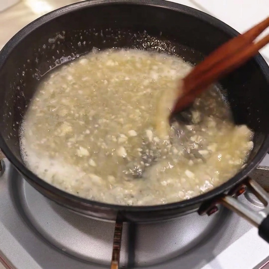 Butter melting into a bubbling pan sauce while being stirred with wooden chopsticks.