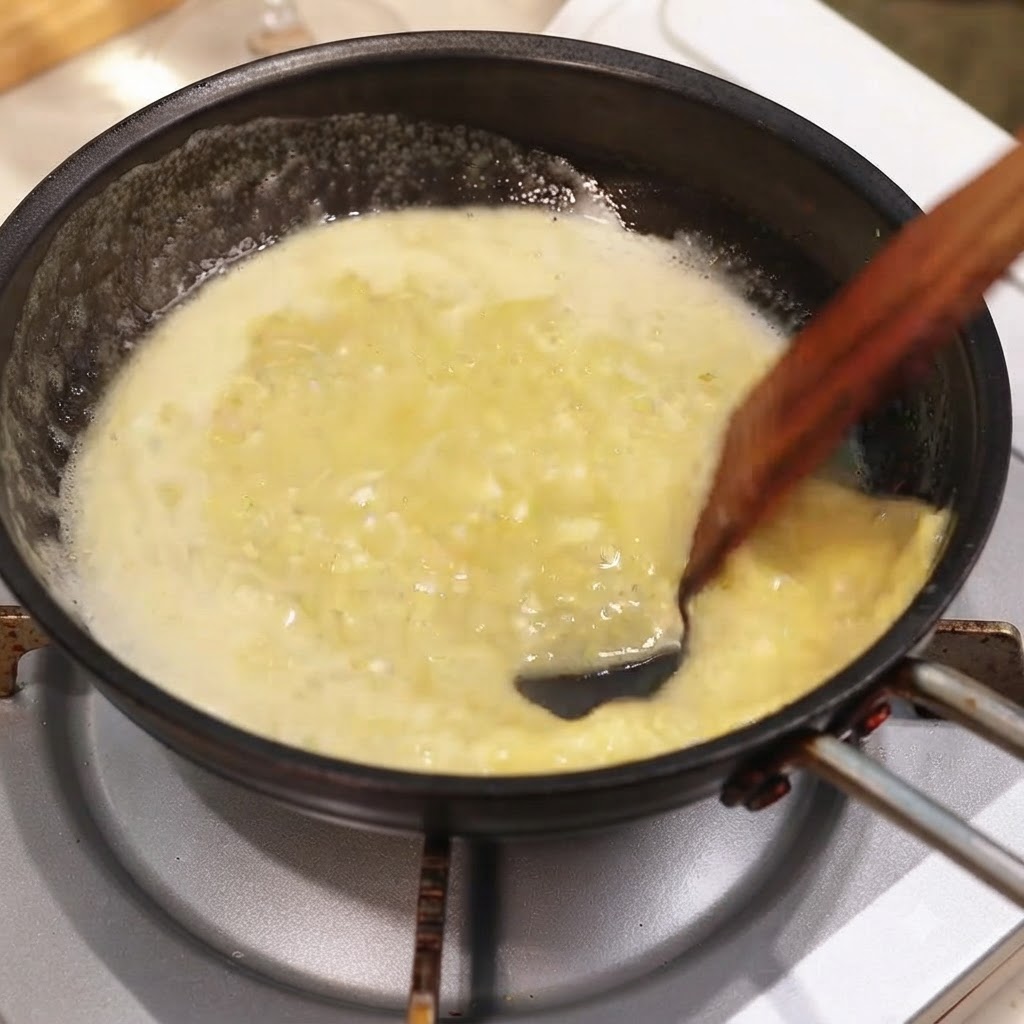 A pan of rich garlic-lemon butter sauce being mixed with chopped herbs using a wooden spatula.