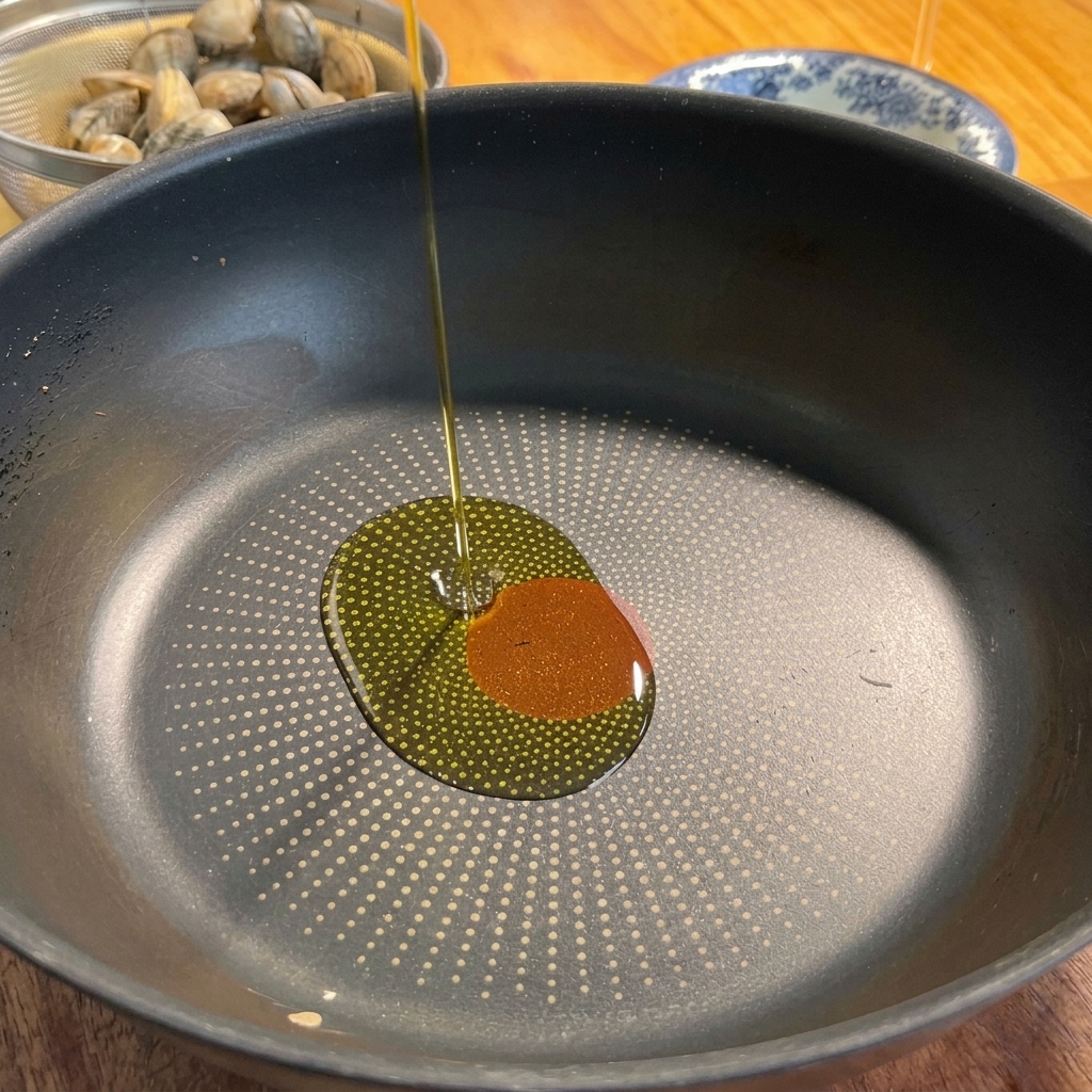 Olive oil being poured into a frying pan alongside garlic and chili pepper.