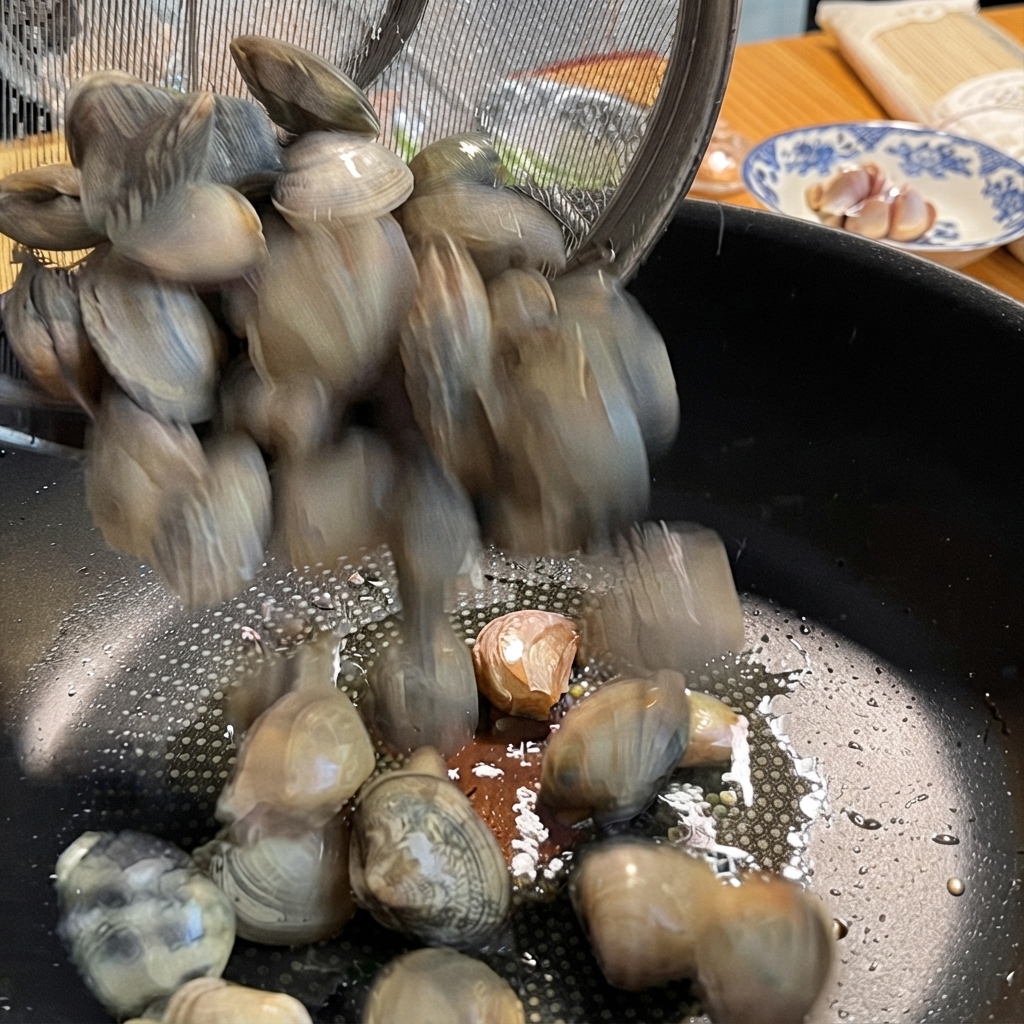 Clams being poured from a metal strainer into a pan with garlic.