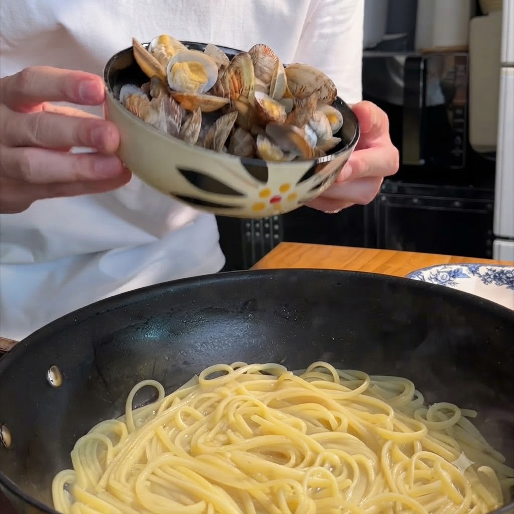 A person holding a patterned bowl and tipping cooked clams into a frying pan filled with spaghetti.