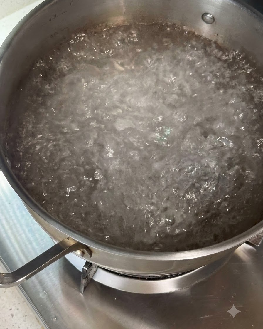 Dry pasta being stirred into a pot of boiling water using utensils.