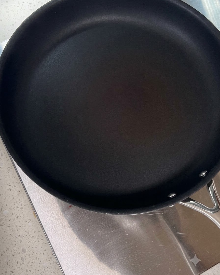 A clean black frying pan heating on a stovetop.