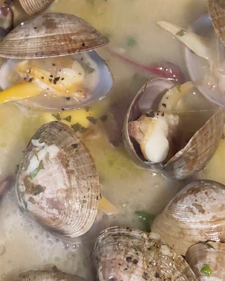 A pan covered with a lid while clams steam and simmer in broth until their shells open.