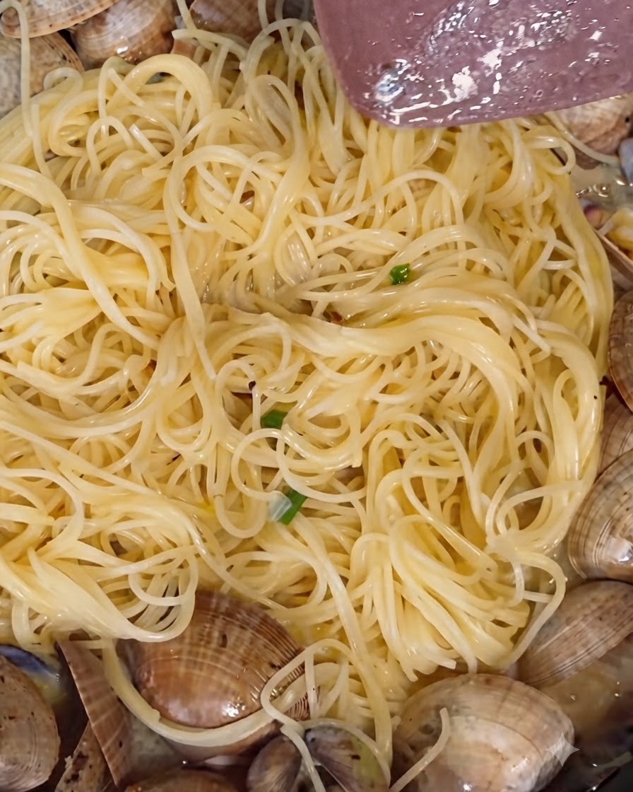 White pepper powder and freshly ground black pepper being sprinkled over simmering clams in a pan.