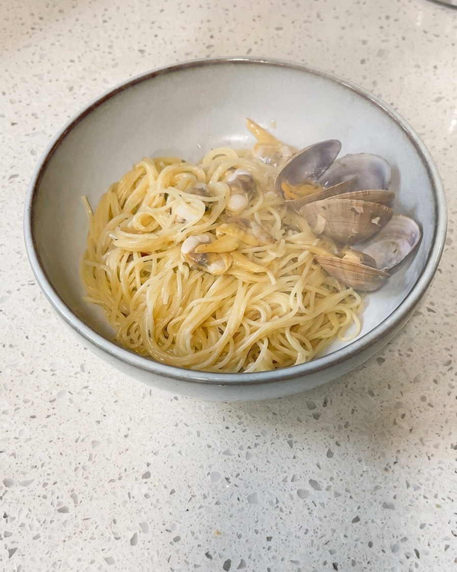 Small pieces of cold butter being dropped into a pan containing cooked clams and broth.
