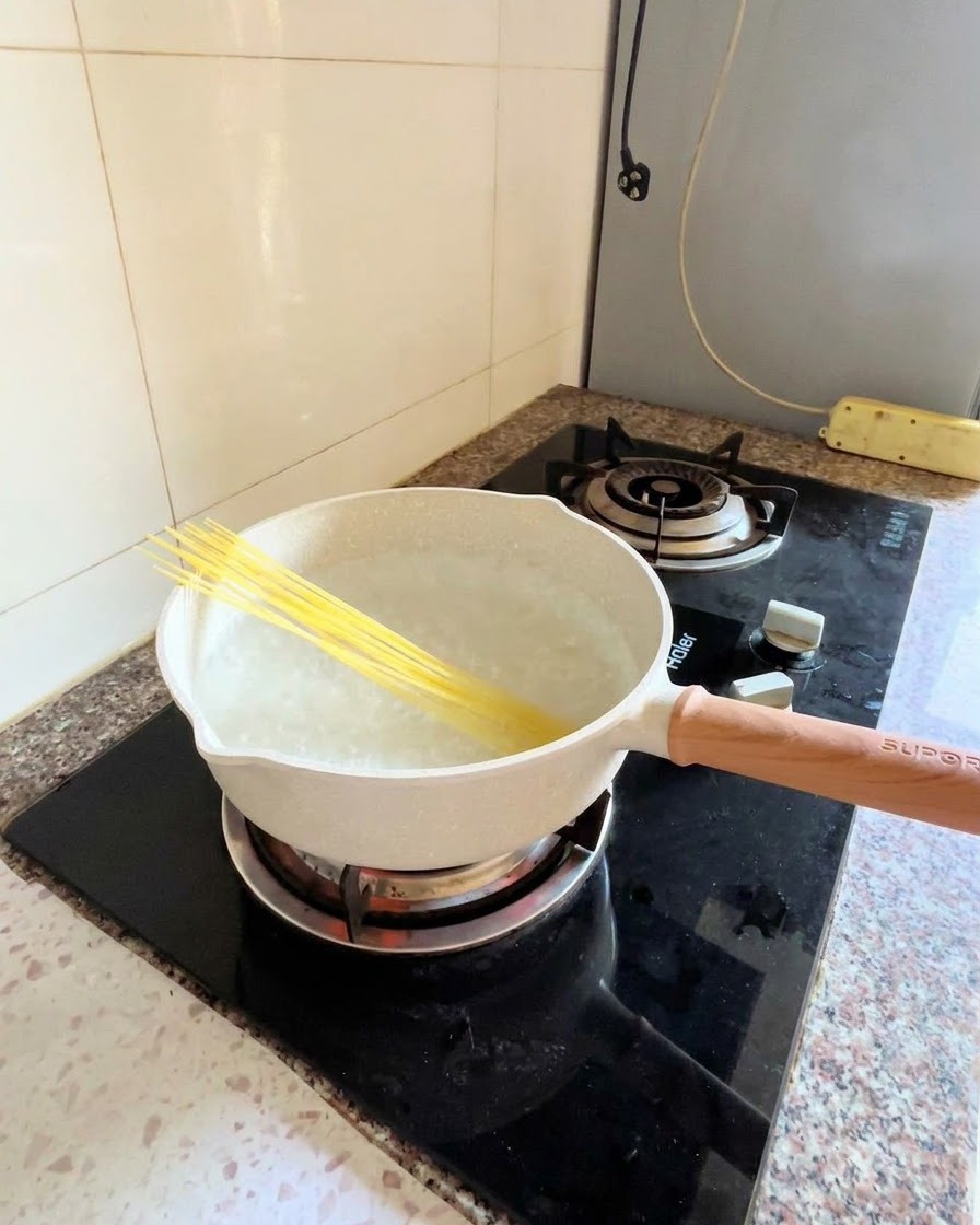 Dry spaghetti noodles placed diagonally into a pot of boiling water on a stovetop.