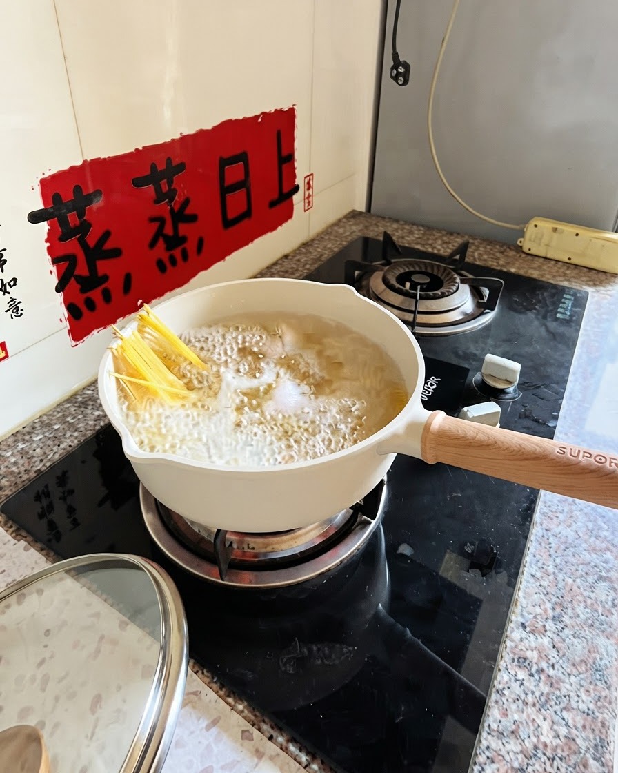 Spaghetti boiling in a white pot with tongs partially submerging the noodles.