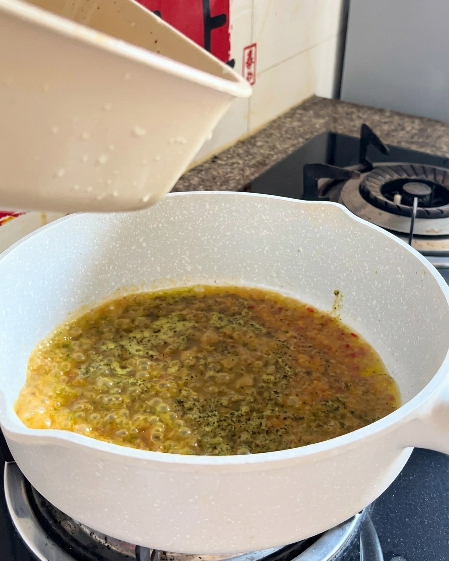 Cooked spaghetti and liquid being combined in a pan during the final toss.