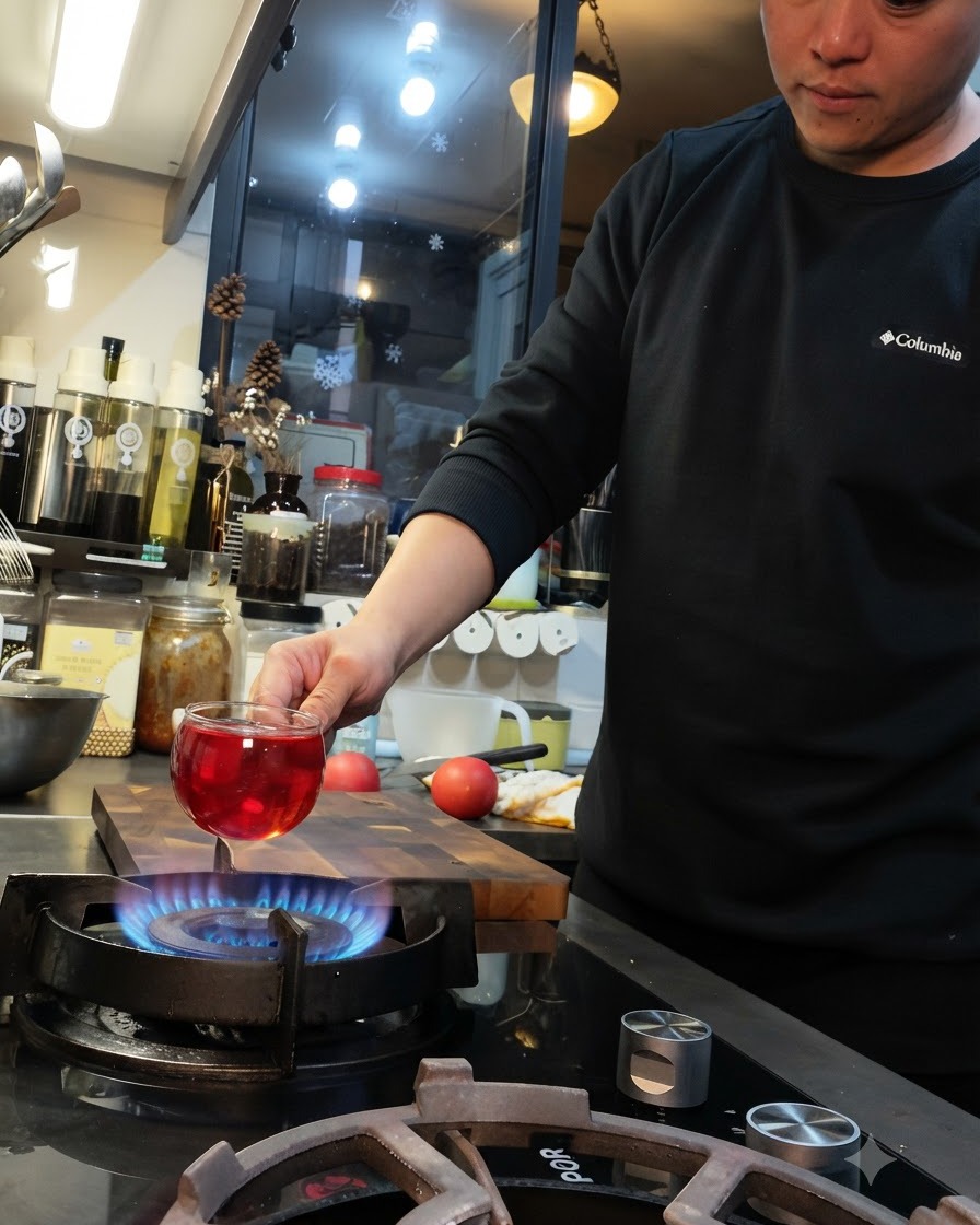 A tomato held over a blue gas stove flame with a cross cut on its surface.