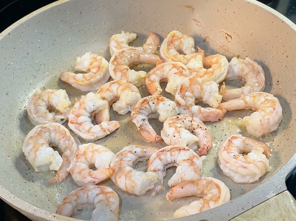 Shrimp frying in a pan with black pepper sprinkled over them.