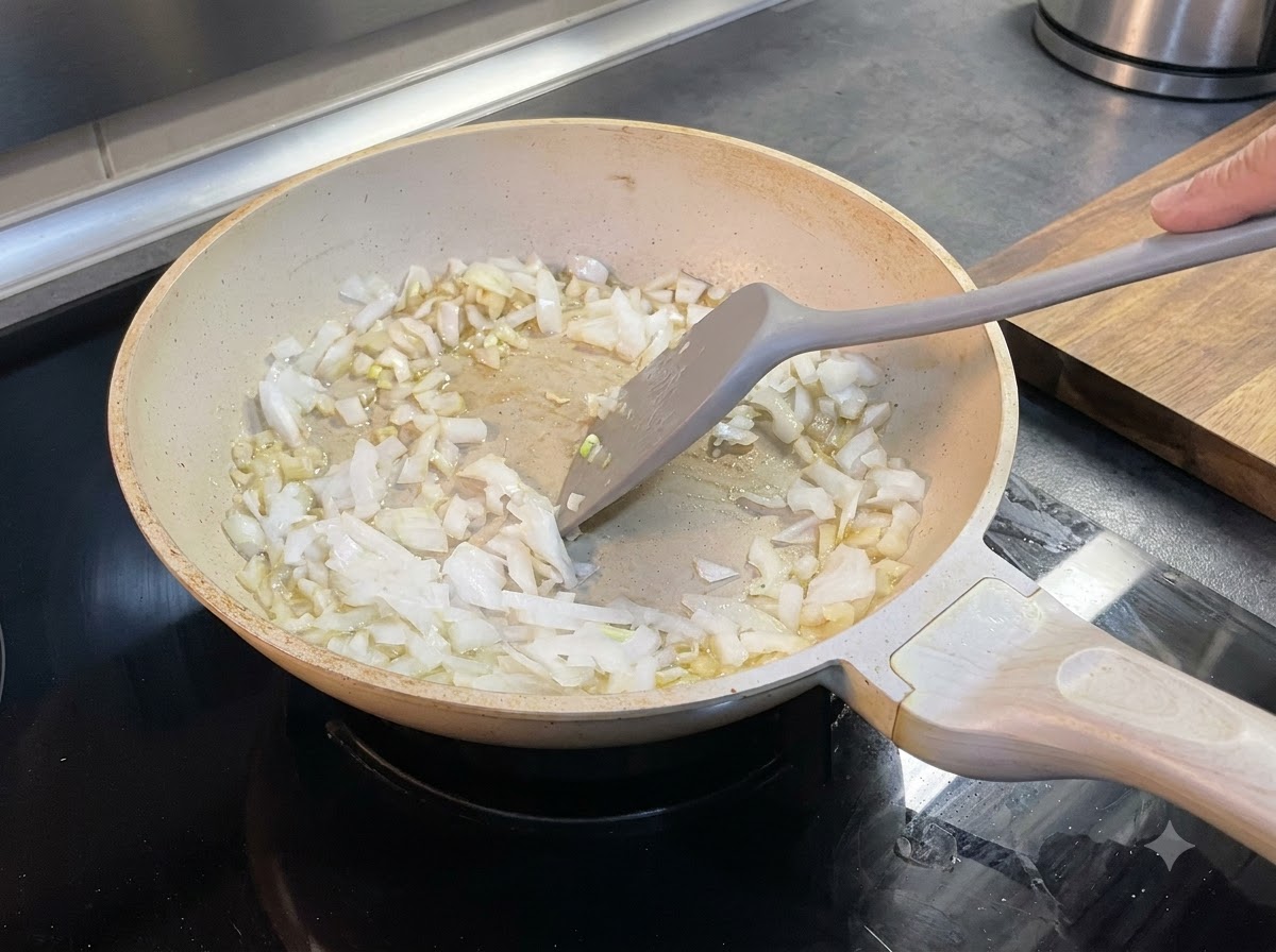 Chopped onions being stirred into melted butter inside a pan using a spatula.