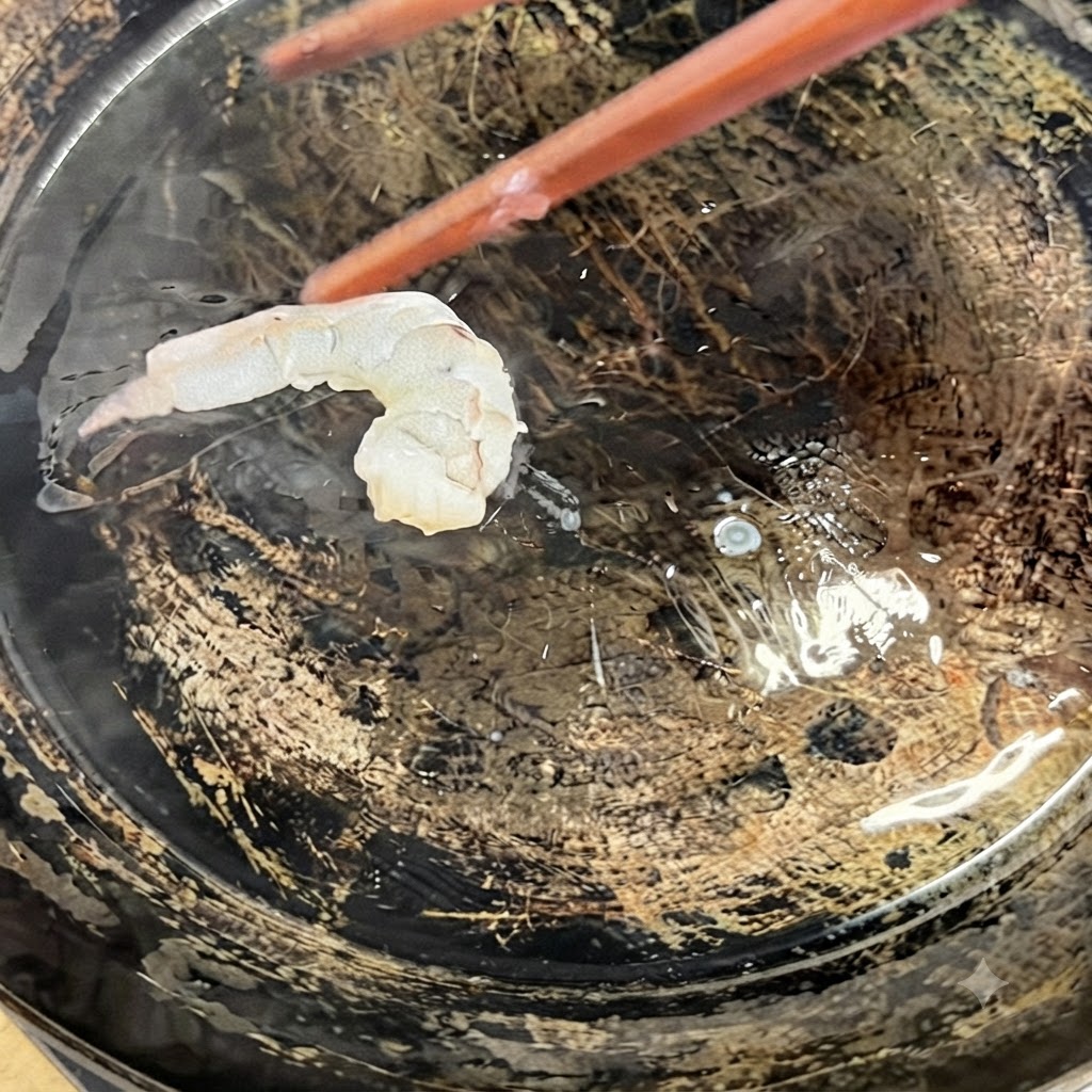 Butterflied shrimp being placed into a hot oiled skillet using cooking chopsticks.