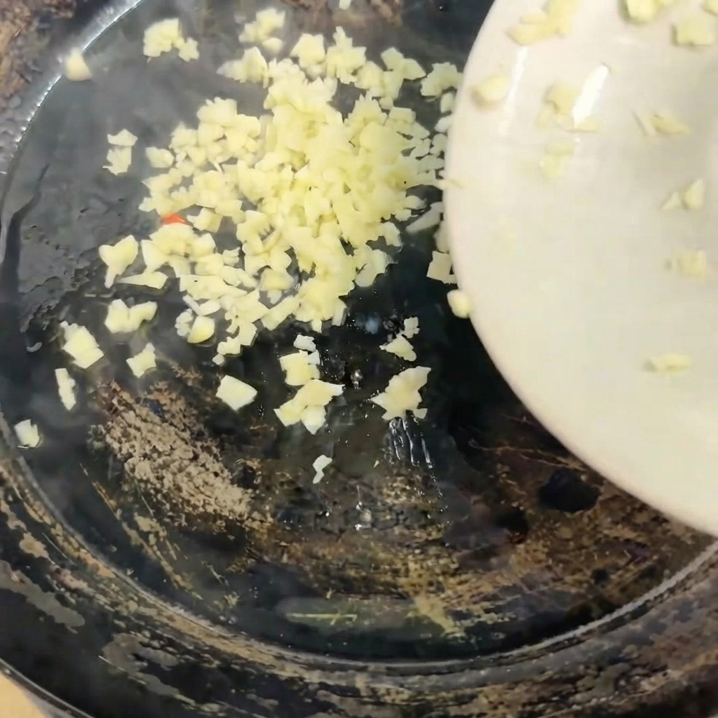Minced garlic being poured from a white plate into a hot skillet.