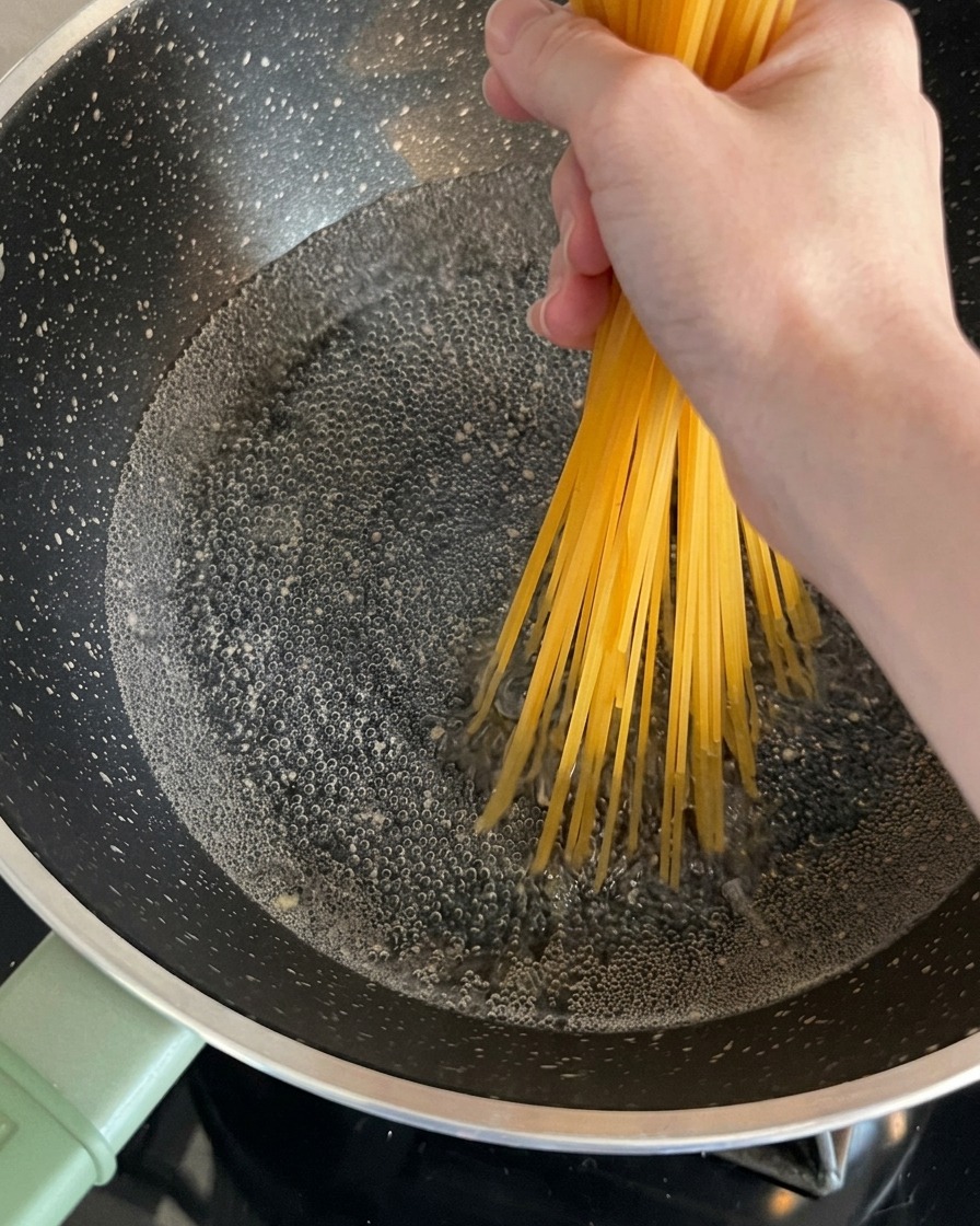 Dry spaghetti noodles being held by a hand and placed into a bubbling pot of water.