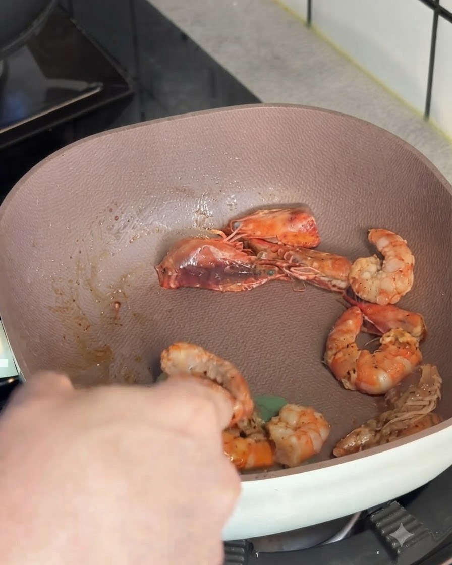Sautéed pink shrimp being lifted out of a shallow pan with a cooking utensil.