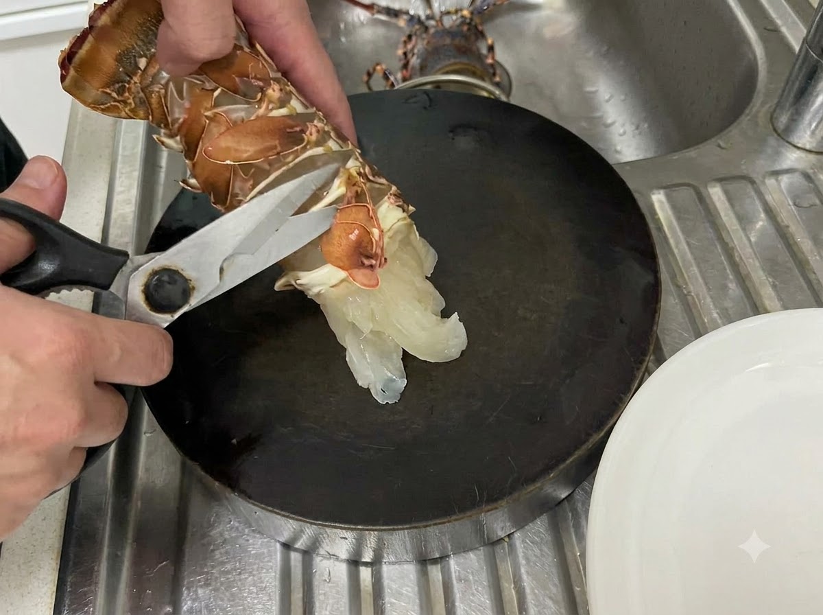 Hands using kitchen shears to cut along the bottom membrane of a raw lobster tail over a dark cutting surface.