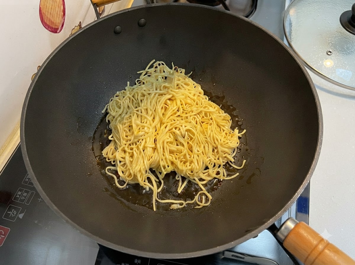 Drained E-fu noodles being stir-fried in a black wok using a spatula.