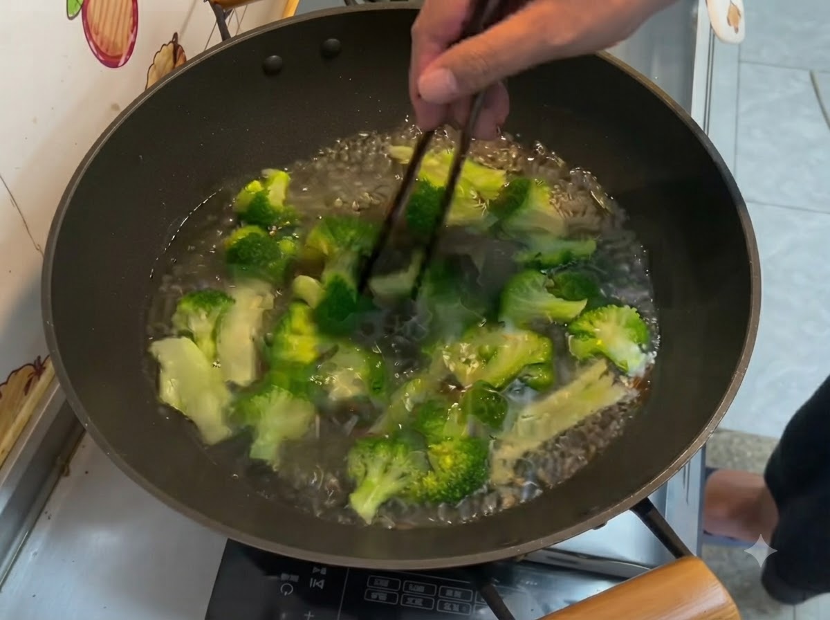 Bright green broccoli florets boiling in water inside a wok, stirred with chopsticks.